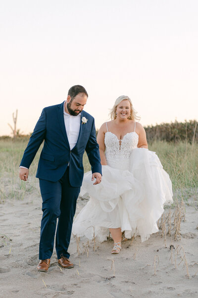 happy bride and groom walking in beach dunes