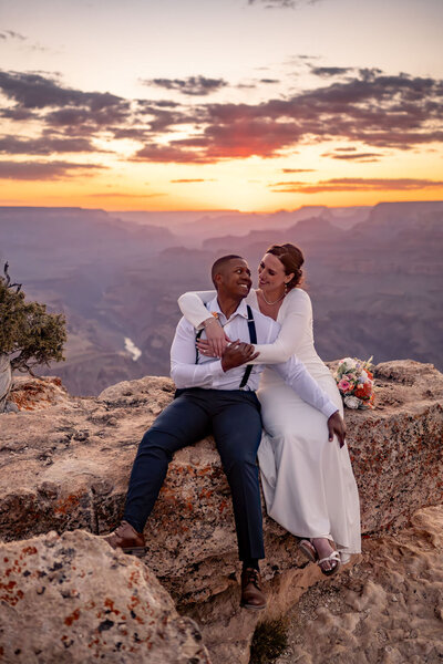 A couple celebrating their elopement on the Grand Canyon’s rim, holding hands with the expansive canyon view behind them.