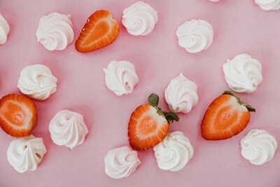 halved strawberries and dollops of whipped cream against a pale pink background