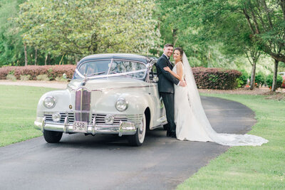 Bride and groom leaning against classic car for wedding portraits