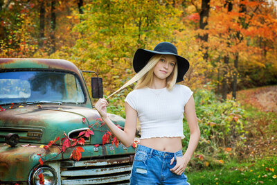 High School senior girl wearing blue dress and tan hat standing on a bike path in the middle of summer.