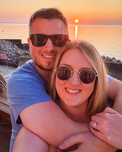 picture of married couple in front of a sunset by the water