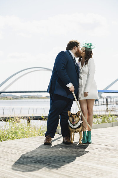 A couple kissing with their dog standing between their legs