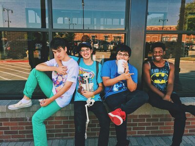 4 diverse teen boys sitting on window ledge with fountain drinks