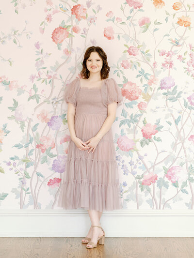Headshot of Rachel in a light pink dress in front of a floral wall