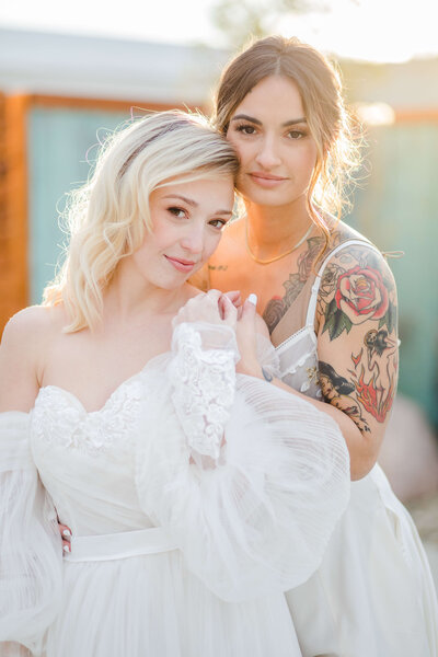 two brides who just got married, holding hands as they gaze at the camera. the sunset is setting behind them. taken at mojave east in cincinnati.