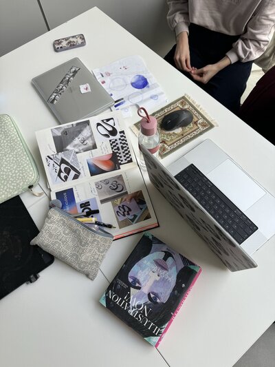 a top down shot of a messy desk. It has a laptop, journal, book and pencils scattered around
