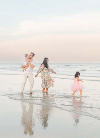 A family candidly dancing near the water's edge during sunset captured beautifully by a Hilton Head Family Photographer, Lamp and Light Photography.