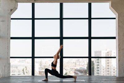 Woman in low lunge pose doing yoga in front of a large window