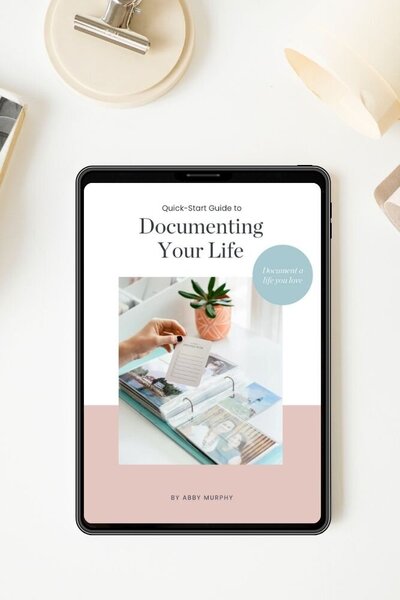 Laptop, tablet, cup of coffee, and a pen on a table with Abby Murphy's free download: 18 Brand Photoshoot Ideas for business owners on the tablet screen