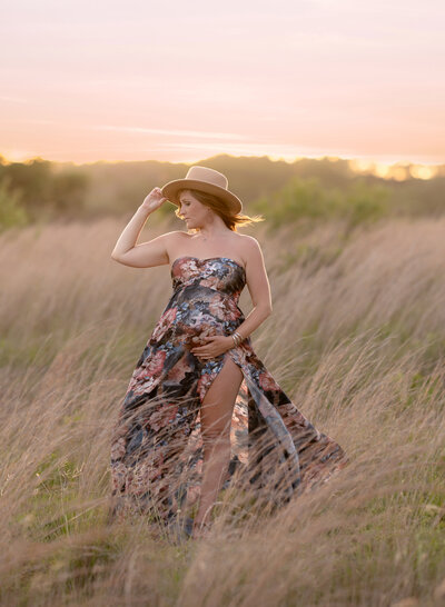 Pregnant woman wearing a hat and floral dress in a grassy field