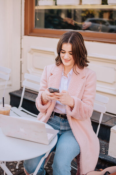 Madison sitting at a table outside with laptop on iphone