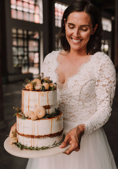 Bride smiling and holding a two-tiered wedding cake.