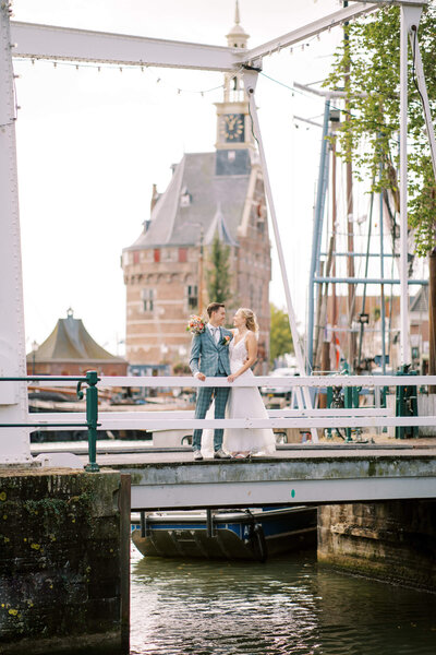 Een elegant bruidspaar poseert op een brug met een kasteel en water als sprookjesachtig decor.