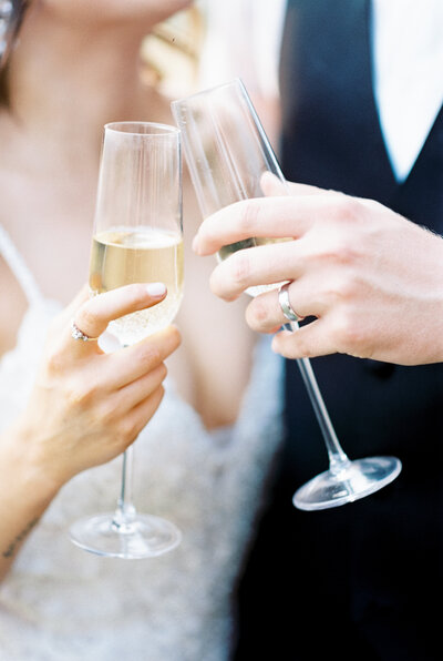 Fine art film photo of a bride and groom doing a cheers with champagne glasses at the