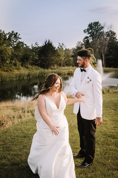 Bride and groom holding hands running pass a water fountain on a pond.