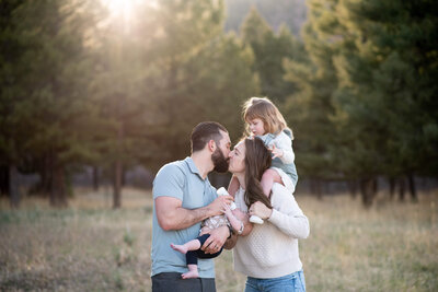 Happy parents kiss while feeding newborn and toddler on mom's shoulders