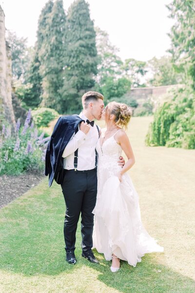 Bride and Groom are standing in front of Syon Park , looking back over their shoulder towards the camera. The bride is wearing a white lace dress with a long veil and the groom is in a black tux