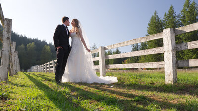 bride and groom smiling at each other while standing in a field next to a picket fence