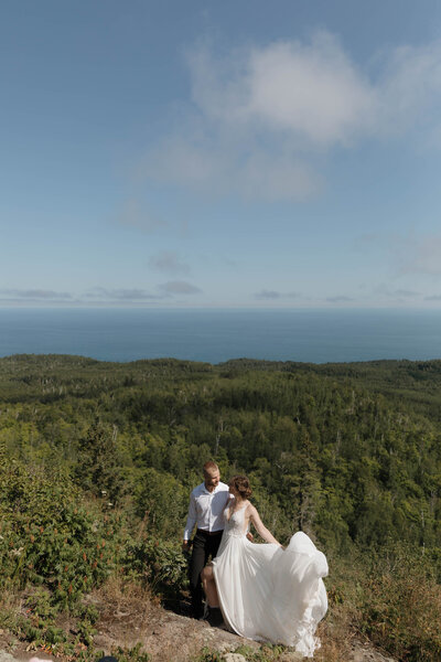 A newlywed couple with their arms around each other as they walk on a trail 