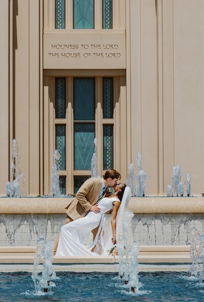 bride and groom share a kiss in front of fountain
