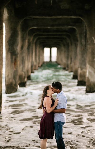Newly engaged couple embracing under a pier on a beach