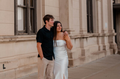 Couple stands together staring off into the distance in an urban setting.
