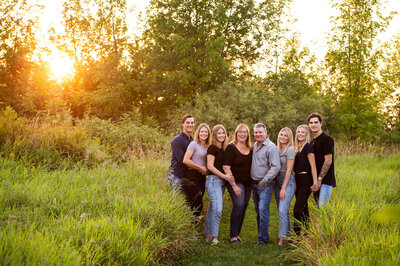 mom and dad with their adult children and  boyfriends in a grassy filed at sunset captured by Ottawa Family Photographer JEMMAN Photography
