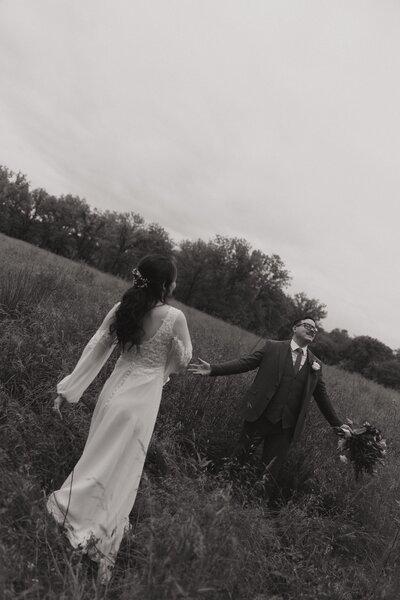 Couple wanders through a field with outstretched arms