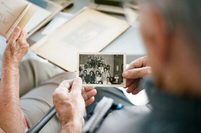 an elderly man holds an old photograph of his family. 