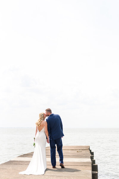 A bride and groom holding hands and walking away from the camera on a pier of Lake Erie.