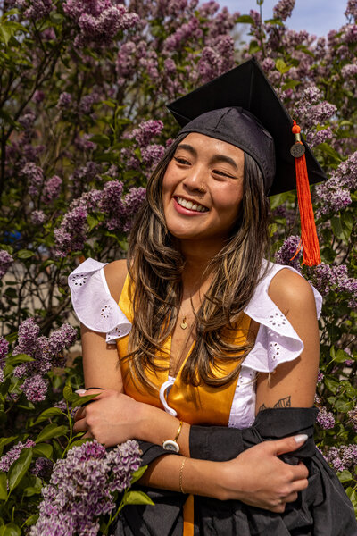 Image of graduate in her cap an gown with her gown shrugged off of her shoulders.