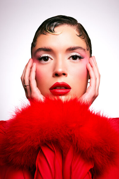 a high end portrait of a woman with high fashion clothes on , wearing red lipstick holding her face