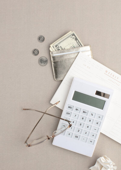 Calculator sitting next to a gold wallet with money sticking out of it