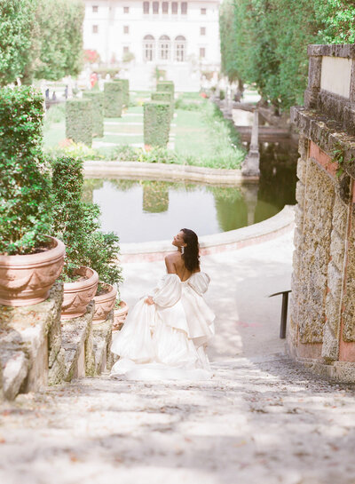 Beautiful bride in ballgown runs down stairs at Vizcaya Gardens in Miami