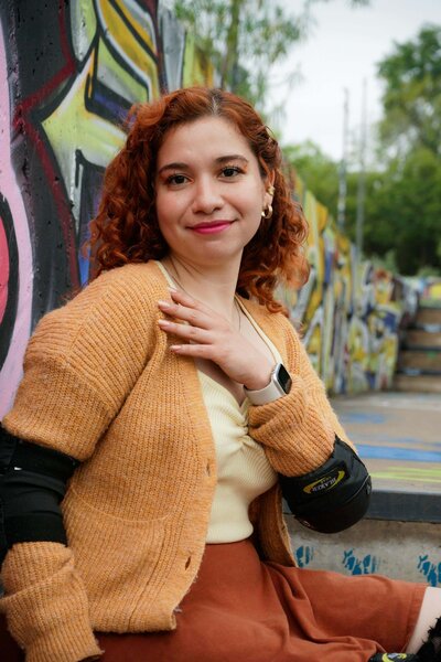 Teen girl with red hair and tan sweater in front of wall with graffiti