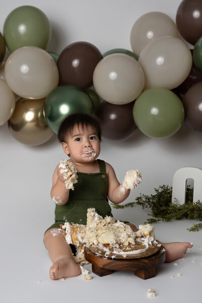 First birthday cake smash photography session in Austin featuring toddler with green balloon decorations