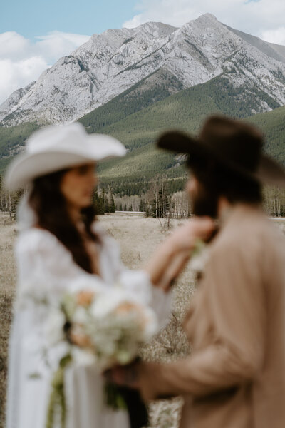 bride and groom in cowboy hats in front of mountain range