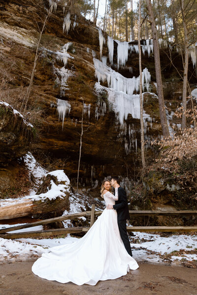 Bride and groom embracing in front of a cliff with icicles.