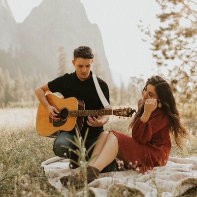 man playing guitar for woman who is sitting in a grass field