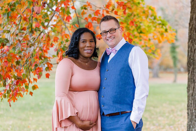 A couple posing in front of the Alexandria, Virginia fall foliage during their maternity portrait session.