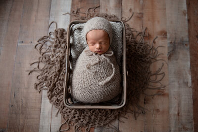 baby wrapped in gray wrap with a bonnet in a a basket at his Detroit Maternity Photography Session