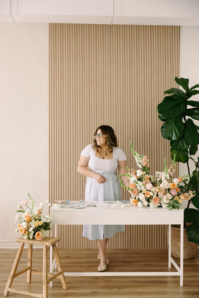 Wedding planner, Zelie & Co., standing behind a desk with orange and white florals with pops of greenery
