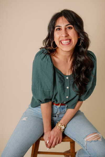 Woman in a teal top and jeans sits on a stool