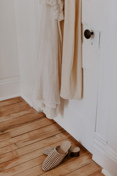 Neutral coloured clothing hanging behind a door with flats on the floor. 