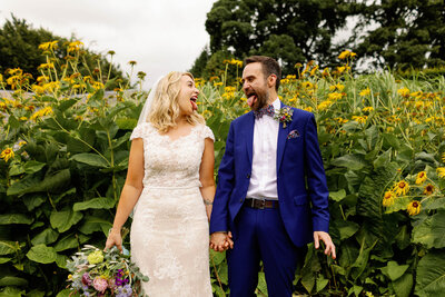 A wedding couple stood in front of a summer meadow at Broughton Sanctuary pulling silly faces at each other