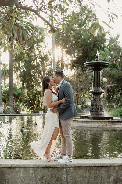 couple standing on a fountain in beverly hills kissing in their engagement photos