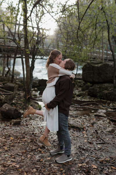 A young and in love couple during their fall engagement session hiking next to a stunning waterfall in Wisconsin