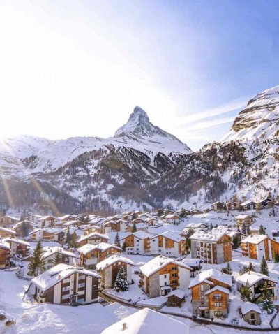 town of zermatt switzerland from a birds eye view. snow capped mountains and homes below the mountain. blue sky.