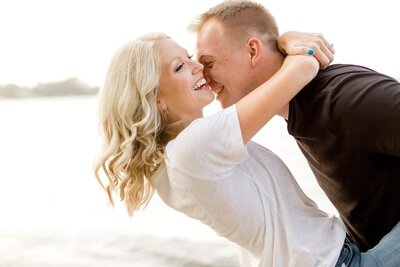 Couple laugh while woman has arms wrapped around man's neck. during engagement photoshoot.